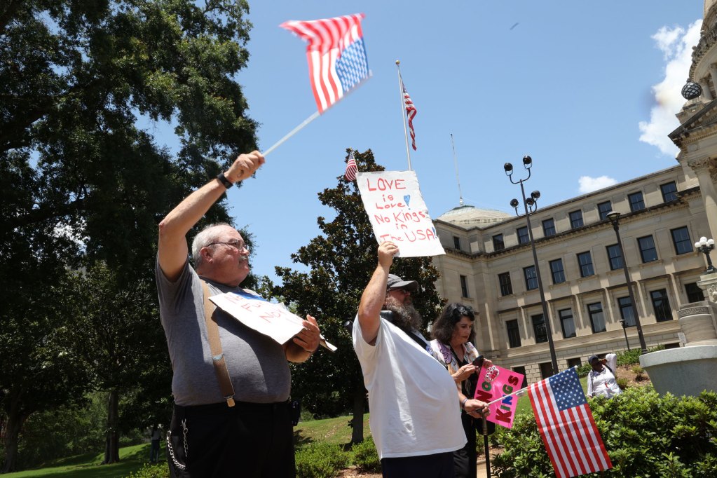 Protesters wave US flags and hold signs, one reads "Love is love, no kings in the USA"