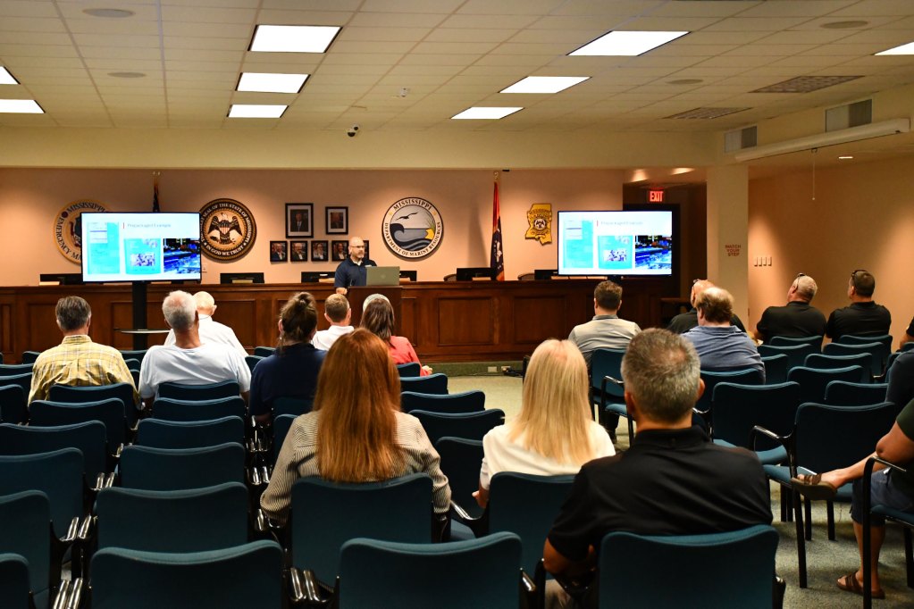 Audience members listen as an MDMR staff member presents slides during a public information session.