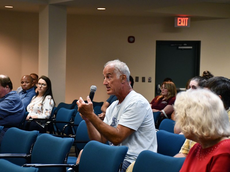 A man in a white shirt holds a microphone while speaking during a seafood labeling Q&A session.