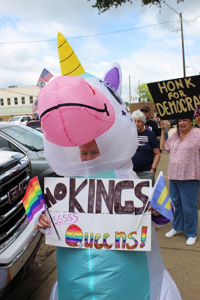 Protesters in an inflatable unicorn suit hold up a sign that reads "No Kings. Yassss queens!"