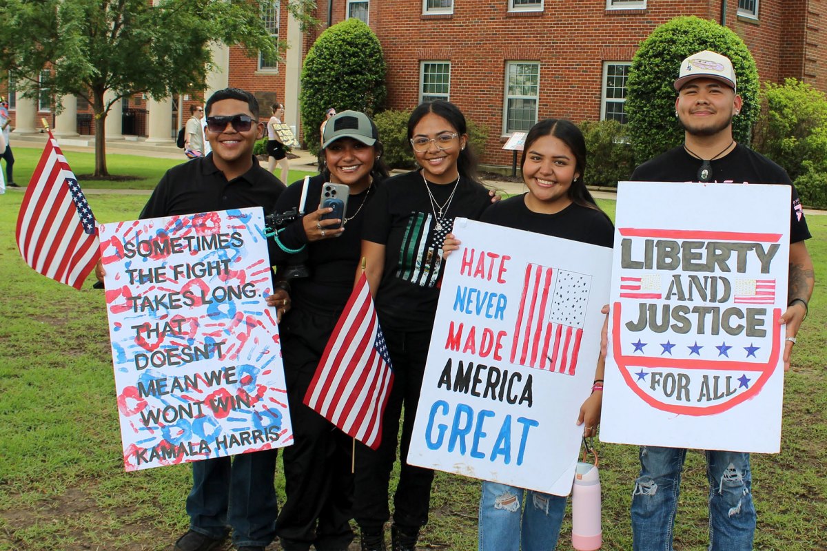 Protesters hold up signs, one reads "Sometimes the fight takes long. That doesn't mean we won't win. Kamala Harris" another "Hate never made America great" and the third "Liberty and Justice for all"
