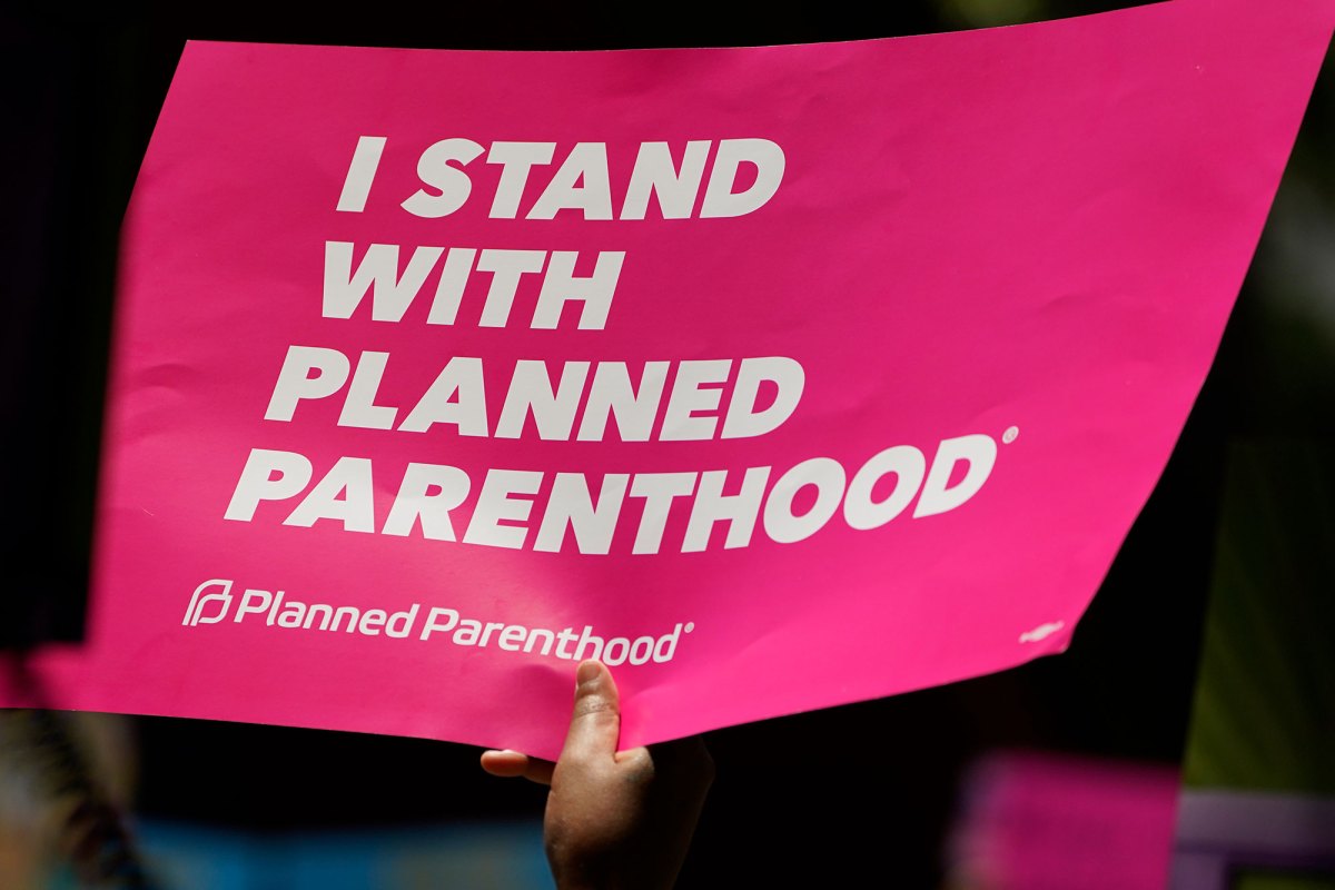A hand holding up a pink sign that reads "I Stand With Planned Parenthood"