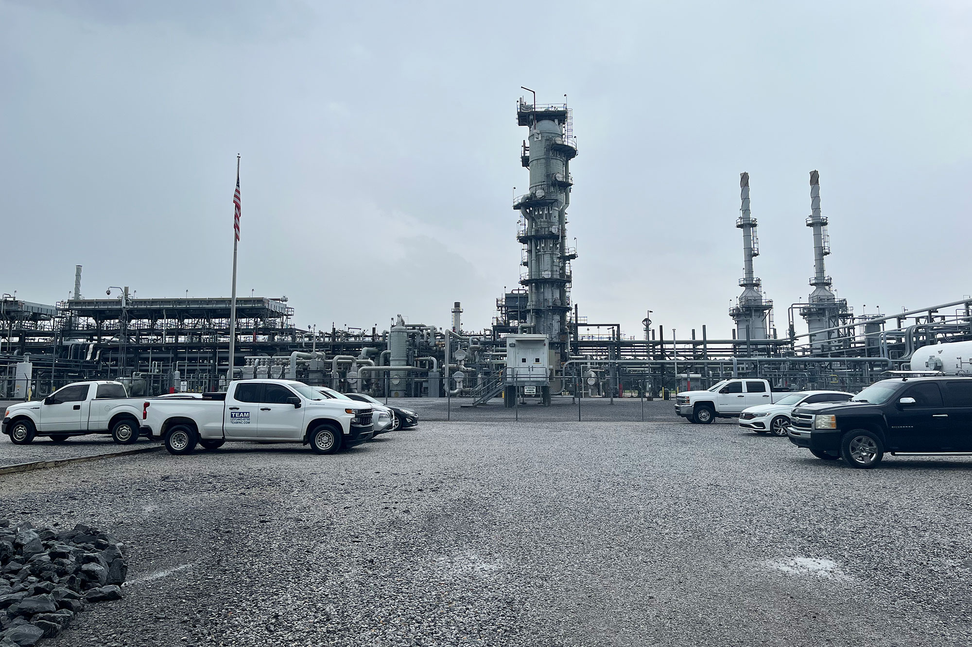 An active oil refinery seen beyond a parking lot full of vehicles