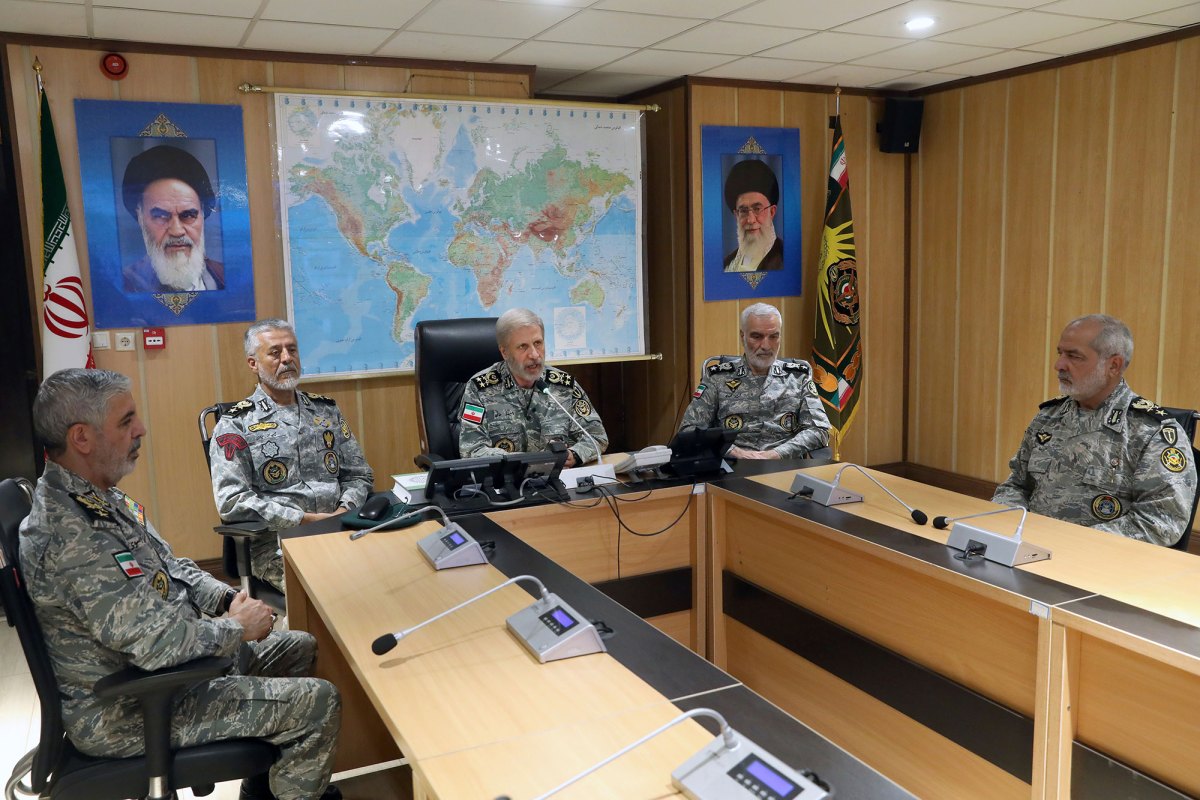 Men in military camouflage uniforms sitting around a desk in a wood paneled room