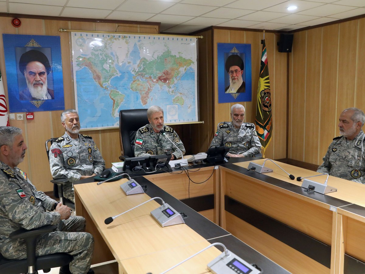 Men in military camouflage uniforms sitting around a desk in a wood paneled room