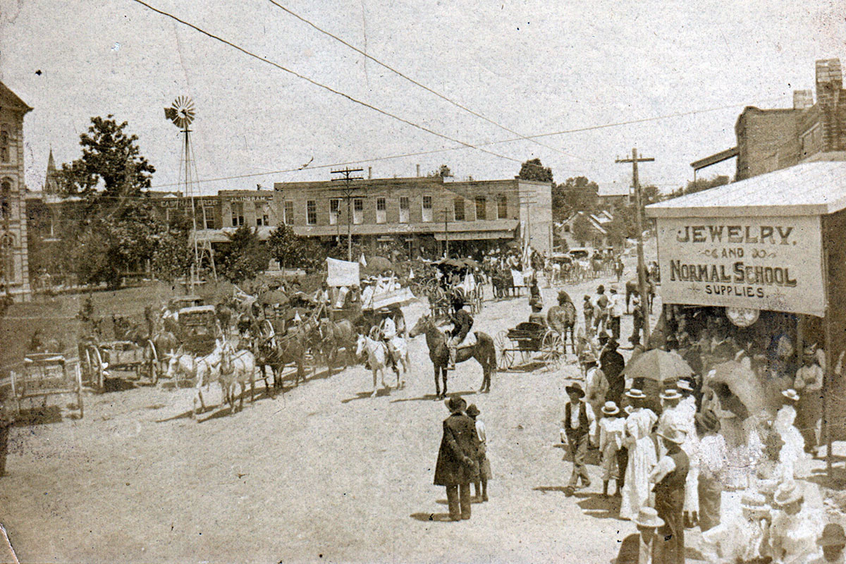 In this black and white image, Black men and women are seen marching along a main street while others are watching.