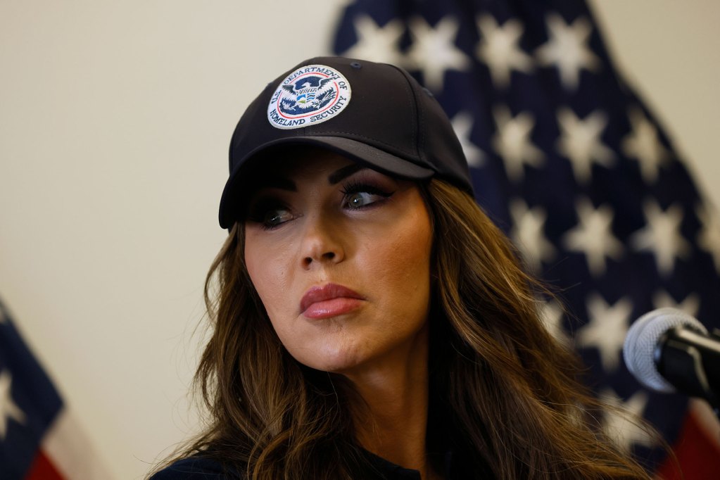 Closeup of Kristi Noem wearing a Department of Homeland Security hat and speaking at a mic