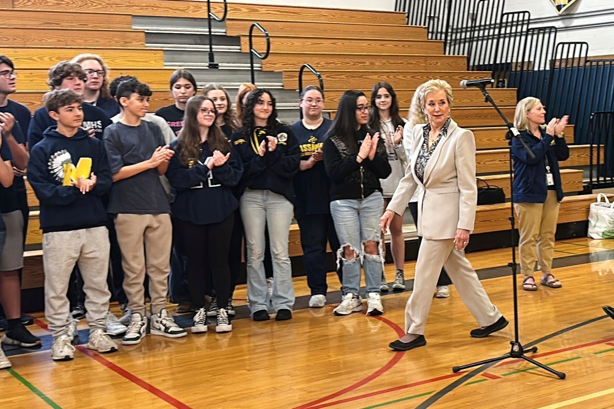Linda McMahon walks past a row of high school students, clapping inside the school gym
