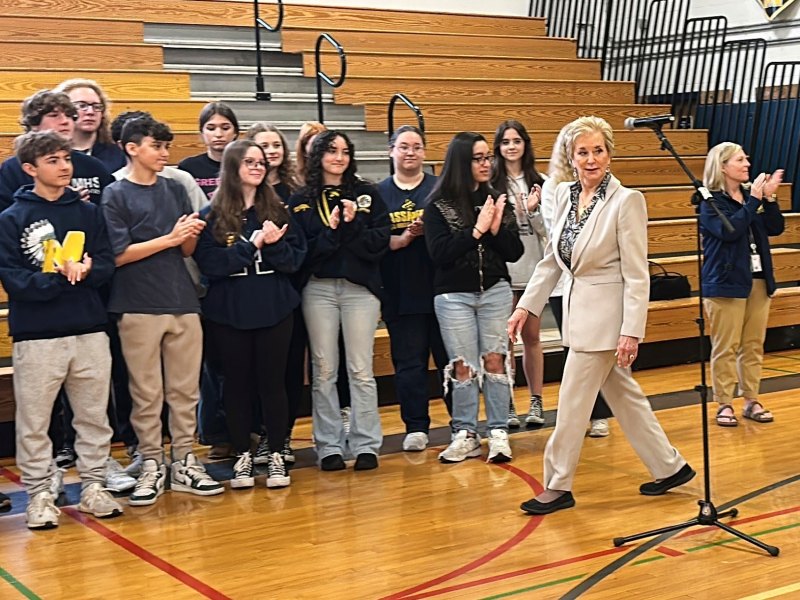 Linda McMahon walks past a row of high school students, clapping inside the school gym