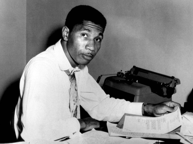 A black and white photo of Medgar Evers sitting at his desk