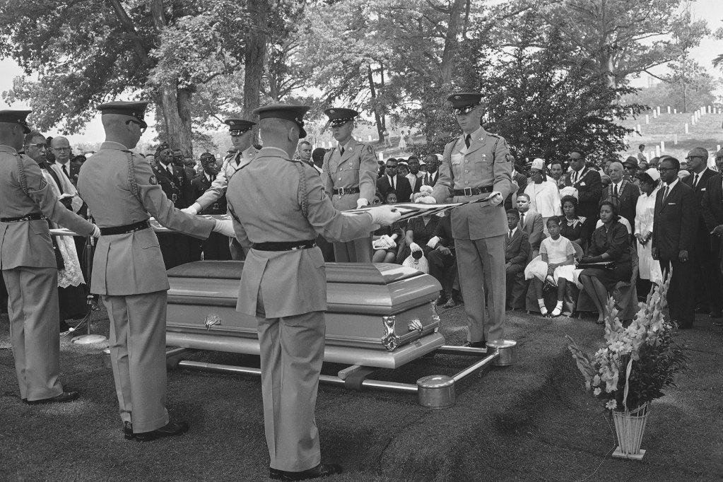 Soldiers fold a US flag over a casket at a funeral