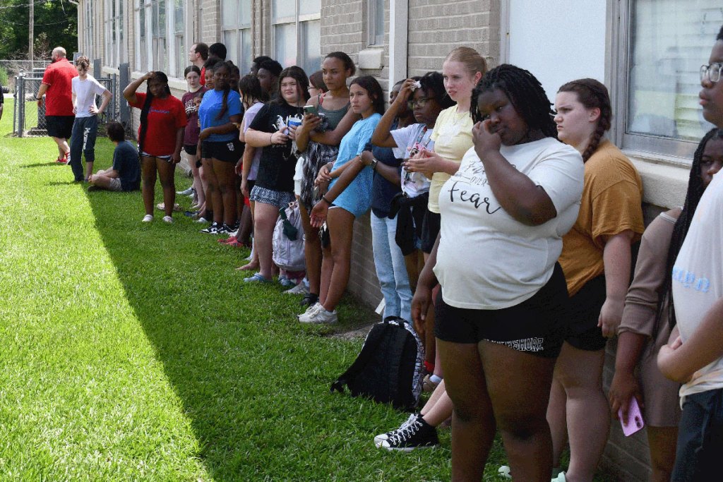 Many students stand in the shade of a nearby building