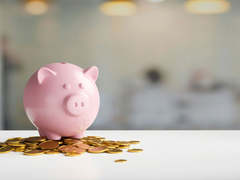 Pink piggy bank standing on top of gold coins