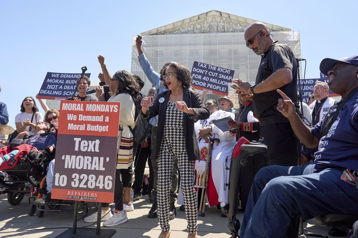 People protest outside of the Supreme Court with signs that read "We demand a moral budget"