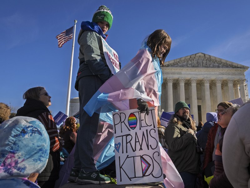 Kids hold hold signs and transgender pride flags outside of the supreme court