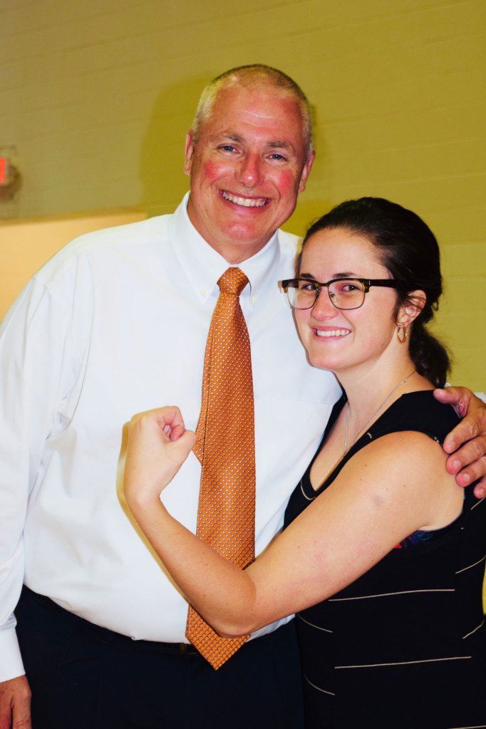 A man and woman stand together, the woman has her arm out in a pose of strength