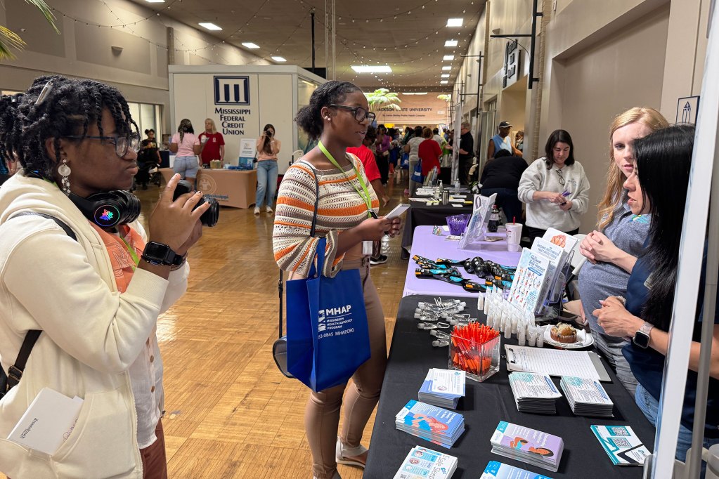 Two students interviewing people behind a table at an event