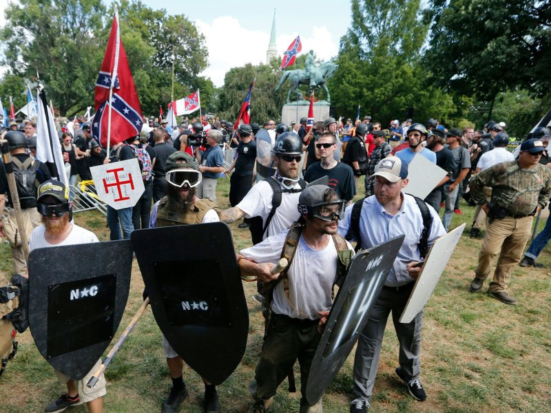 A gathering of demonstrators wearing shields and goggles, others carrying the Confederate flag behind them