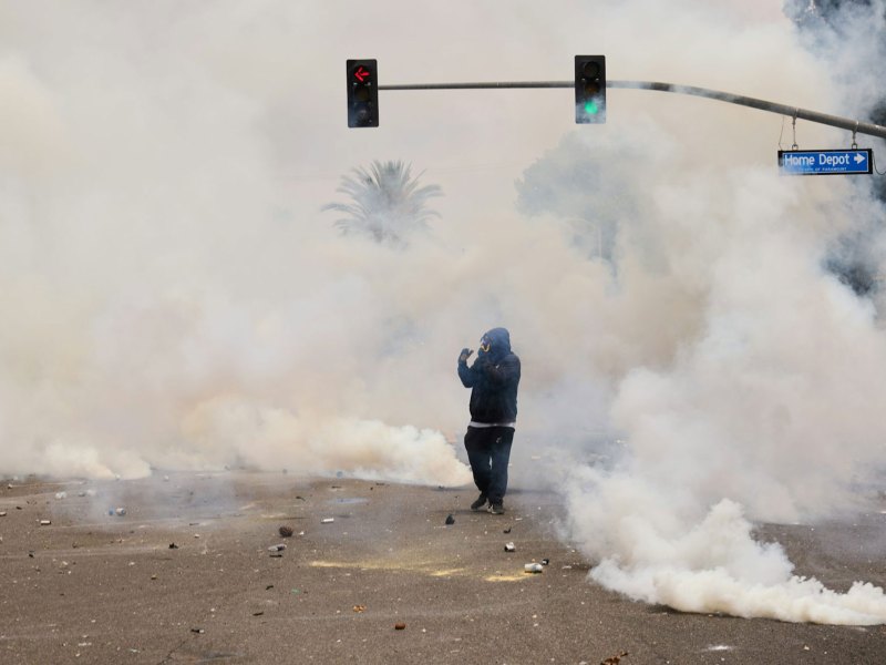 A single person in gas mask walks through a smoke filled road, the street sign reads Home Depot