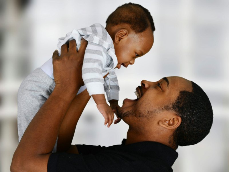 A father lifts his smiling infant up in the air to look at him