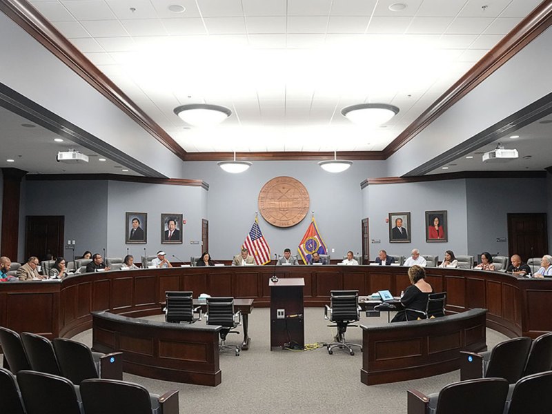 A council room full of people sitting at a long semi circular table
