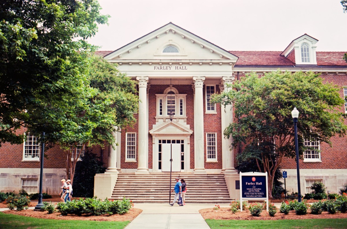 People walk past a campus building labeled Farley Hall