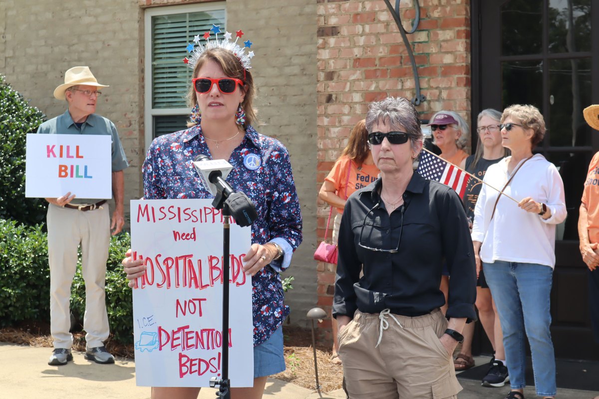 People standing outside of Congressman Michael Guest District Headquarters holding protesting signs