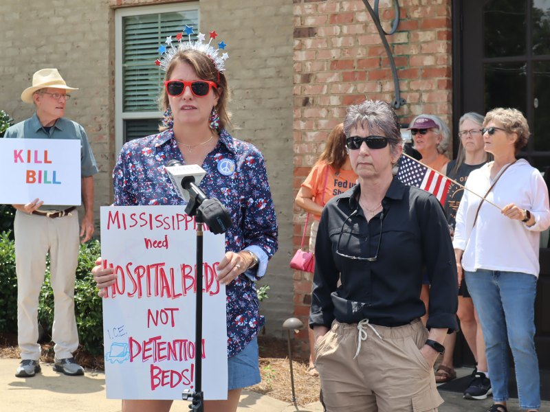 People standing outside of Congressman Michael Guest District Headquarters holding protesting signs