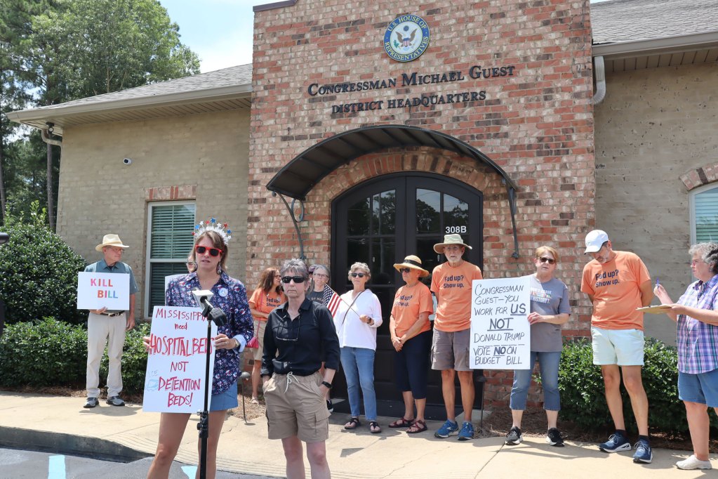 People standing outside of Congressman Michael Guest District Headquarters holding protesting signs