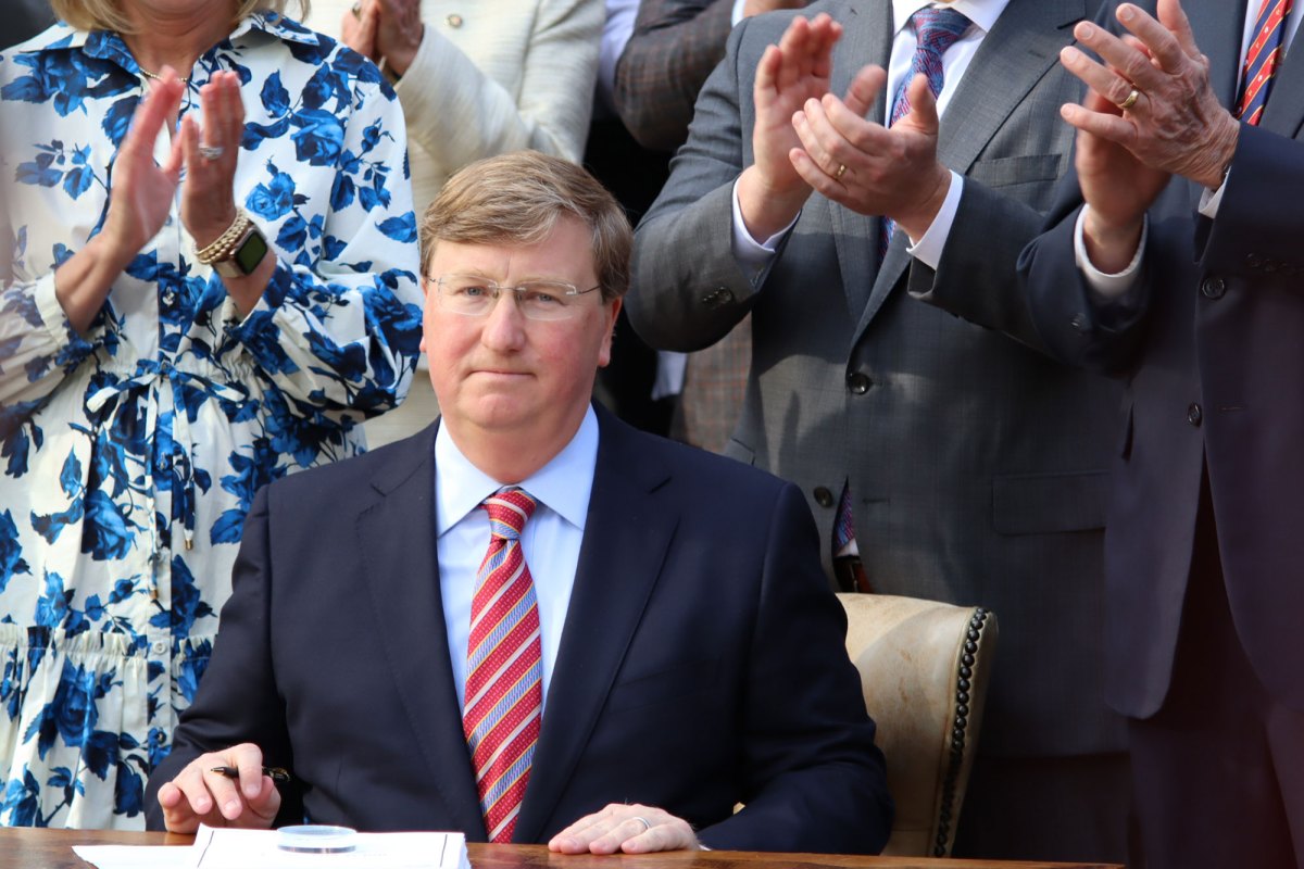 Governor Tate Reeves seated, ready to sign a bill as others watch and clap