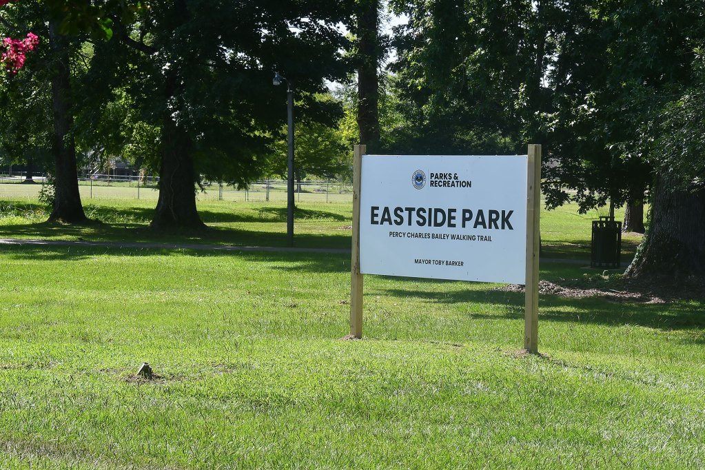 A green space with trees further back and a big white sign that reads Eastside Park