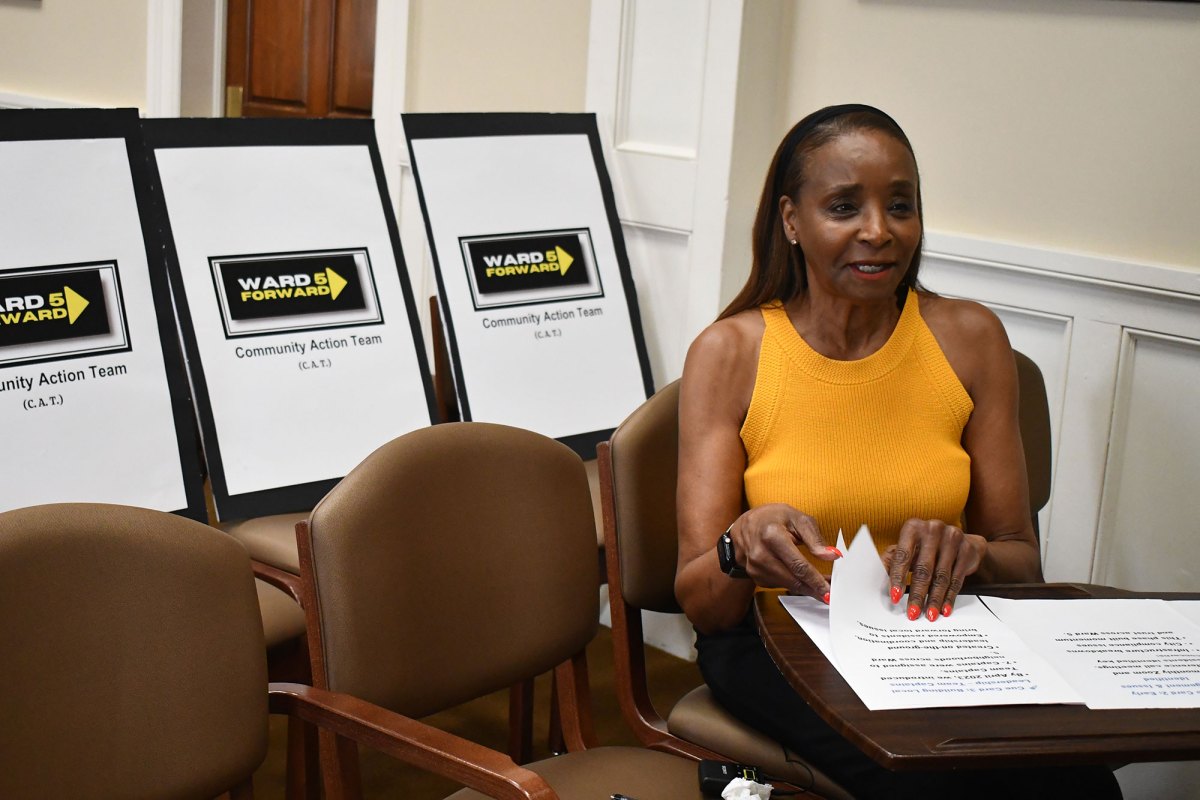 A woman in a yellow top pages through papers. Signs behind her read Ward 5 Forward