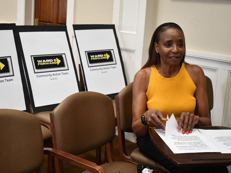 A woman in a yellow top pages through papers. Signs behind her read Ward 5 Forward