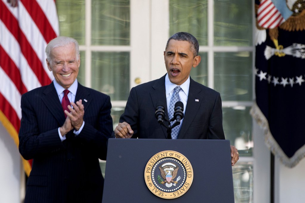 Barack Obama speaks at a podium as Joe Biden claps