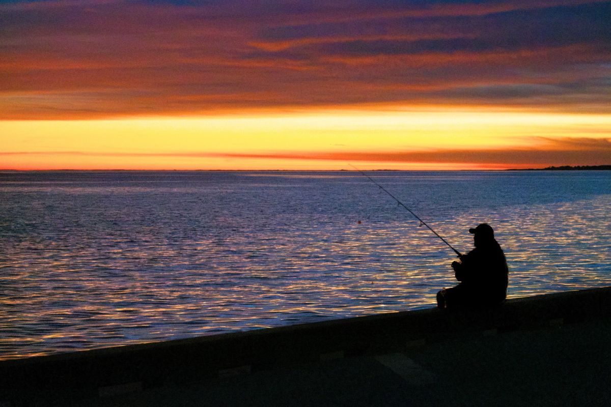 A man fishes in a lake at sunset