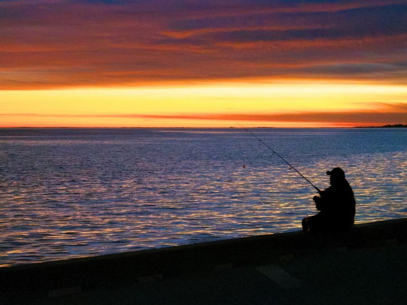A man fishes in a lake at sunset
