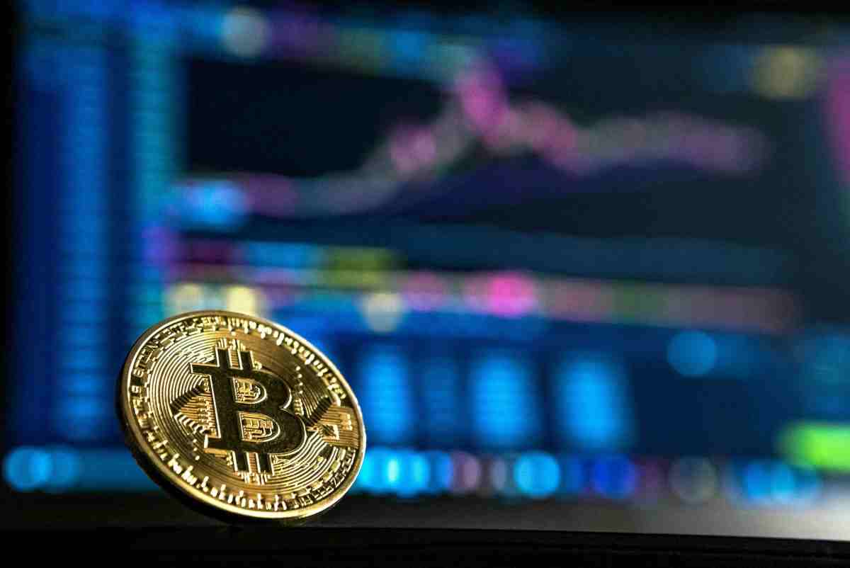 A gold bitcoin seen in front of a blurry computer screen