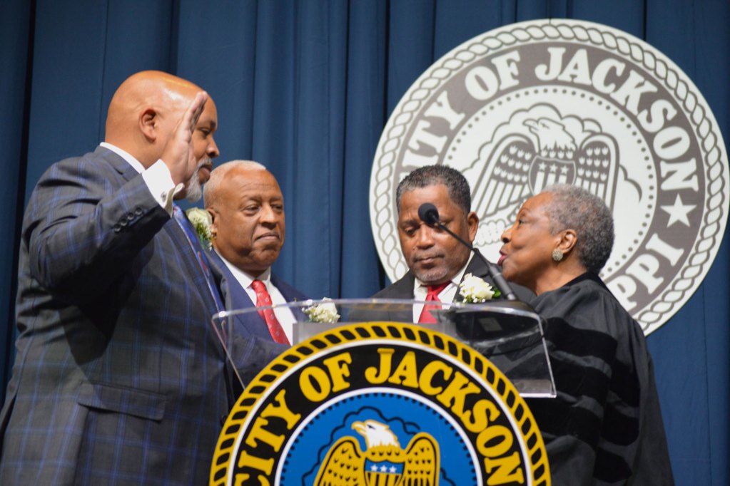 Councilman Brian Grizell wearing a grey and blue stripped suit stands with family while being sworn in by a judge wearing a black robe