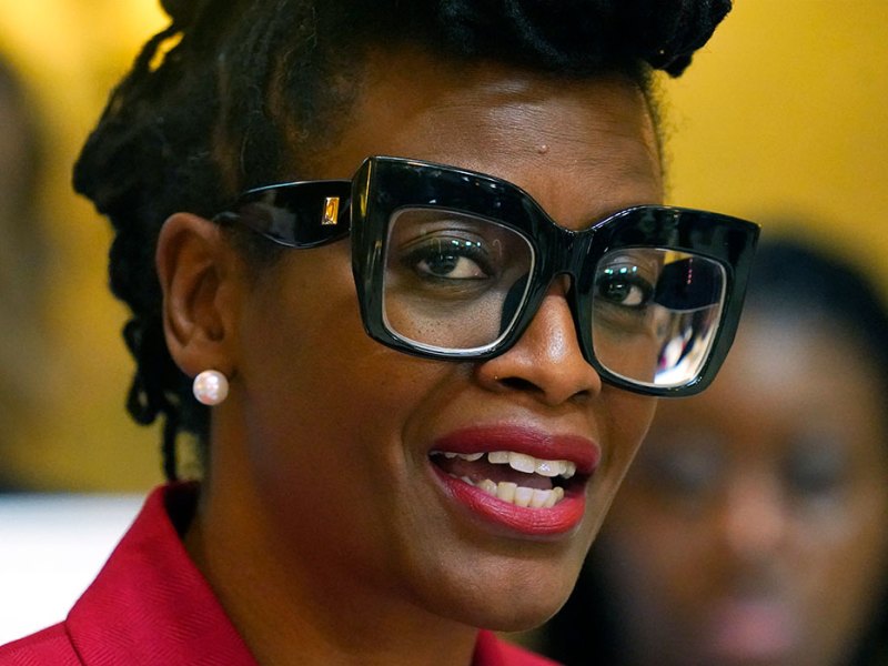 A closeup of a woman in a red top and black glasses speaking