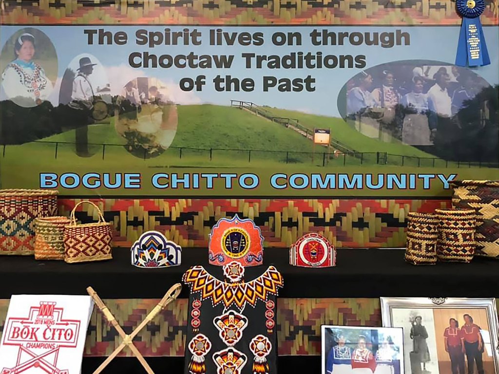 Choctaw cultural booth for the Bogue Chitto community including a colorful background and various items on a tiered, decorated surface.