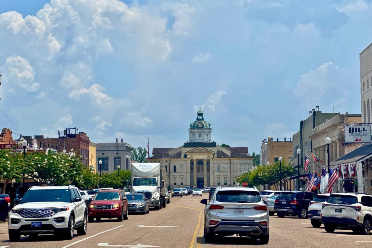 Cars fill a wide two way road, a courthouse visible in the background