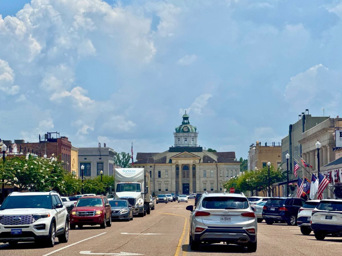 Cars fill a wide two way road, a courthouse visible in the background