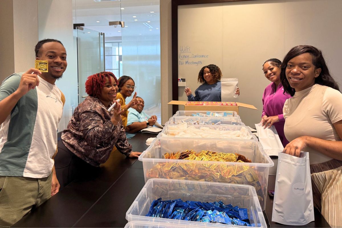 Several people stand around a large table and sort condoms out of large bins and into small bags