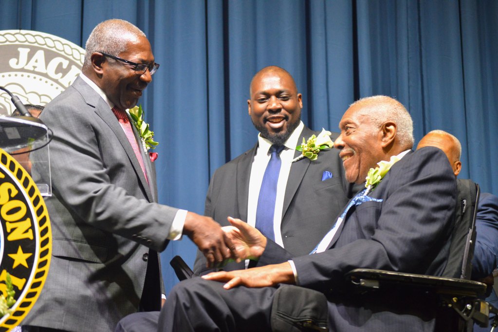 Mayor John Horhn wearing a grey suit shakes the hand of his father Charlie Horhn wearing a navy pinstripe suit