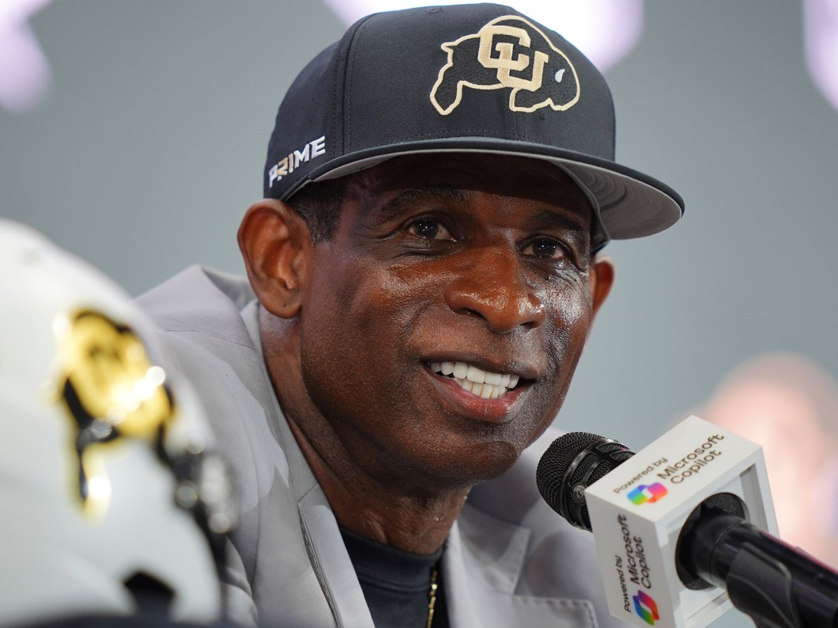 A closeup of Deion Sanders speaking into a microphone at a press conference