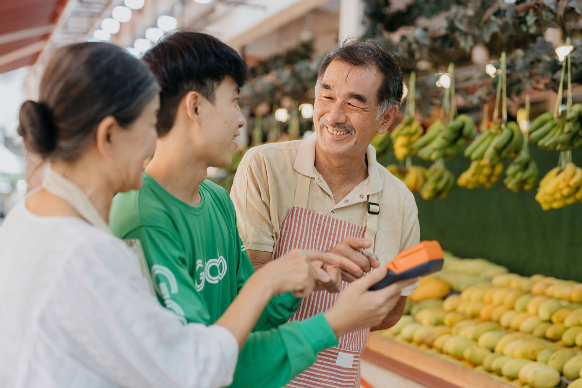 An older couple show a calculator to a younger person in a produce section of a store