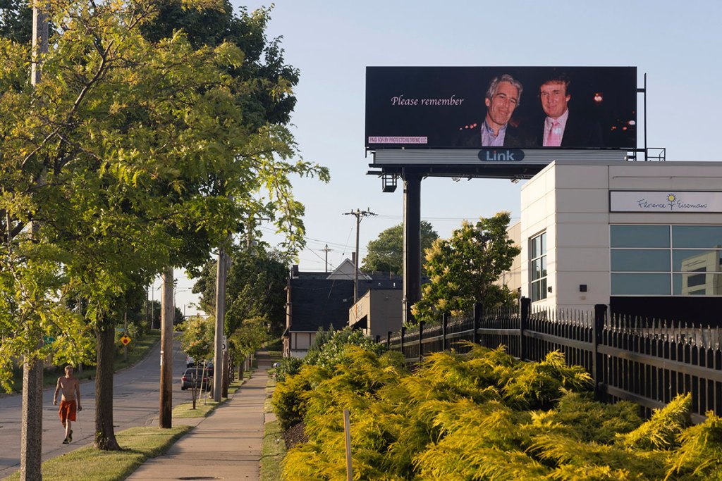 A person jogs past a billboard with Jeffrey Epstein and Donald Trump with the text 'Please remember'