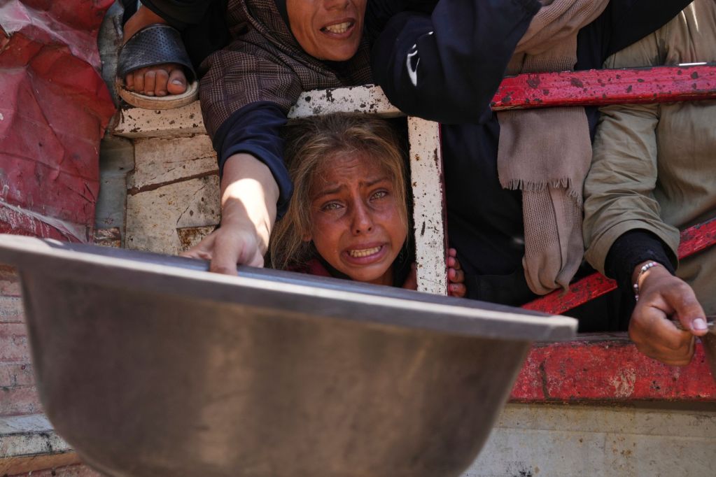 A crying woman's face is seen between the arms of other people, outstretched and begging for food