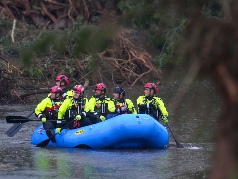 People wearing matching florescent clothing paddle a blue inflated boat down a flooded river