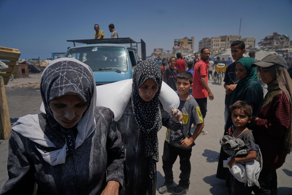 People carry a bag of flower from a humanitarian aid convoy